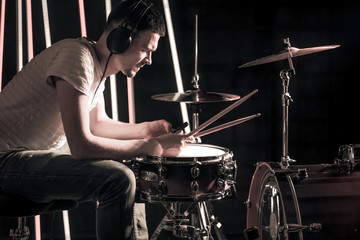 Fototapeta premium Man plays the drums in the headphones. On the background of colored lights.