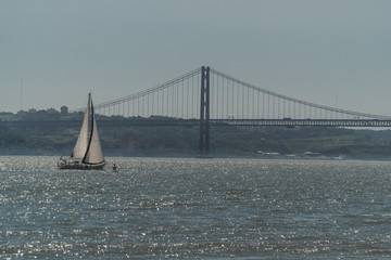 A sailing ship sails through the waters of the Tejo River on the coasts of the city of Lisbon. In the distance you can see the famous bridge of April 25th.
