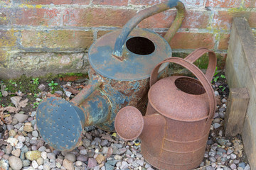two old vintage rusty metal watering cans with stones and bricks in the background