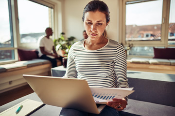 Fototapeta premium Focused young businesswoman working on a laptop and reading pape