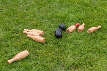 set of fallen traditional wooden skittles outdoors on grass with black balls in summer in UK