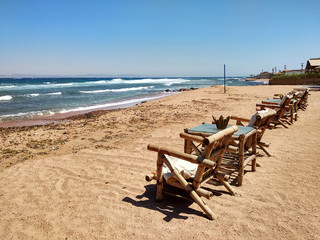 Fototapeta na wymiar Row of bamboo chaise lounge on beach in Dahab, Sinai, Egypt. Beautiful seascape. Relax time.