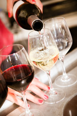 Serving a glass of white wine from a bottle with wine being poured into the bowl of elegant glass