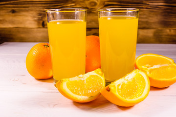 Obraz na płótnie Canvas Oranges and glasses with orange juice on a wooden table