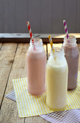 Three bottle of various milkshakes (chocolate, strawberry and vanilla). Healthy smoothie with straw. Tasty milk shake cocktails. Refreshing summer drink. Copy space