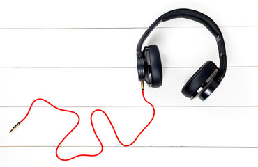 Black headphone and red cable on wood white background.