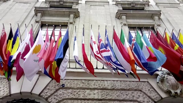 International flags from OSCE and several nations waving in the wind in front of a historical building