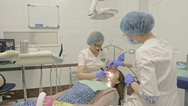 Woman at dentist clinic gets dental treatment to fill a cavity in a tooth. Dental restoration and composite material polymerization with UV light and laser. The doctor works with an assistant.