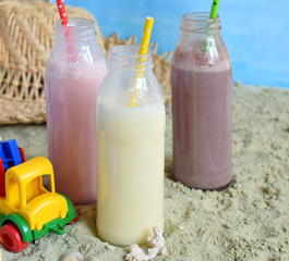Three bottle of various milkshakes (chocolate, strawberry and vanilla). Healthy smoothie with straw. Tasty milk shake cocktails. Refreshing summer drink on yellow sand summer beach. Copy space