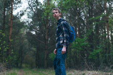 Young man in backpack hiking in dark forest.