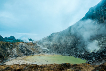 inside view of active indonesian sibayak volcano crater during cloudy day with smoke and rocks