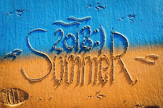 The inscription summer 2018 is written on the colourfull sand. The inscription is made by hand. Blue and yellow postcard.