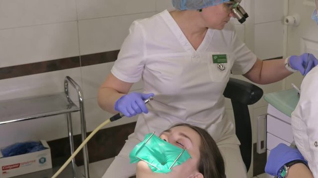 Woman at dentist clinic gets dental treatment to fill a cavity in a tooth. Dental restoration and composite material polymerization with UV light and laser. The doctor works with an assistant.