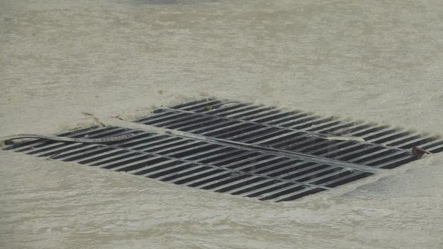 Slow motion, close up dirty water flows into the sewer after heavy rainfall hits tropical town
