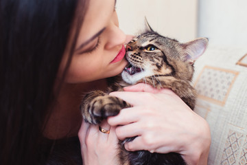 A domestic cat bites a young woman by the chin