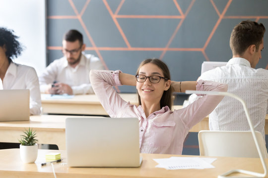 Happy relaxed female student or employee enjoying break resting from work holding hands behind head, young smiling businesswoman breathing air feeling no stress free relief in coworking office room