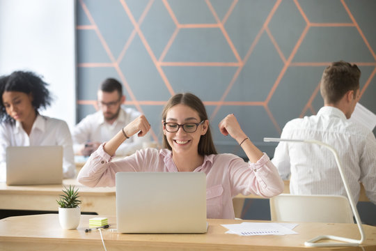 Happy young student or employee feeling excited celebrating good online work result or successful win, motivated by great email news or new opportunity looking at laptop in coworking office room