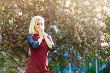 Young pretty girl blowing nose in front of blooming tree. Spring allergy concept