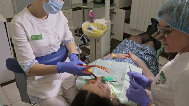 Woman at dentist clinic gets dental treatment to fill a cavity in a tooth. Dental restoration and composite material polymerization with UV light and laser. The doctor works with an assistant.