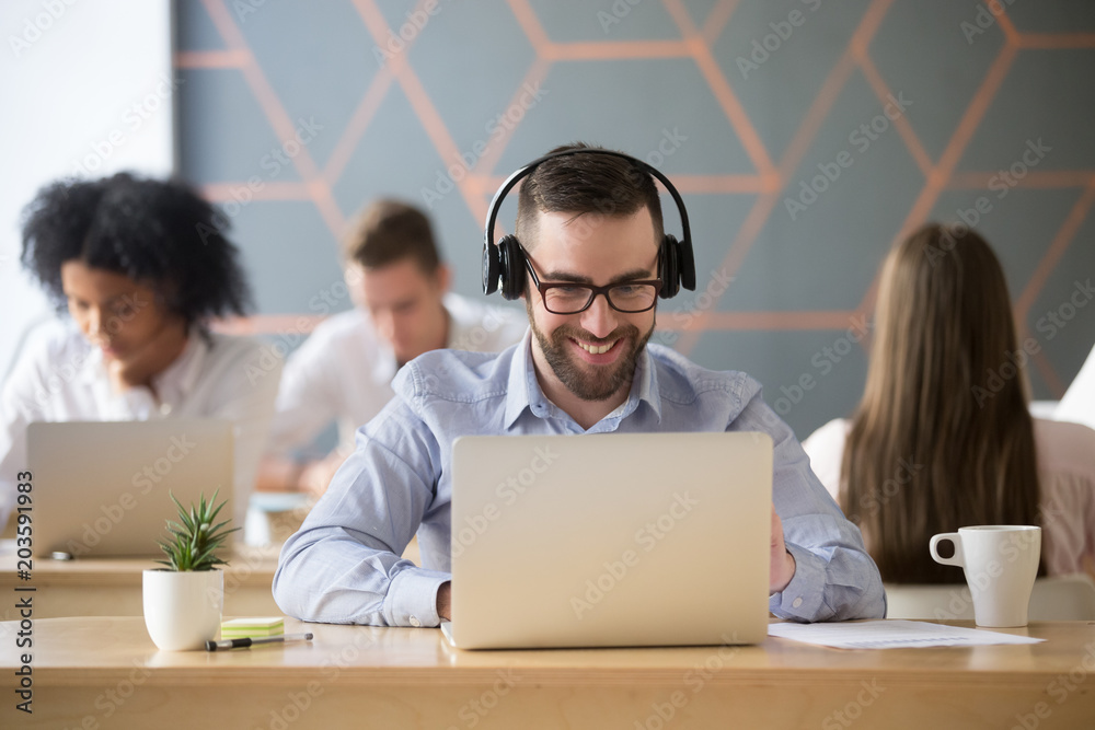 Wall mural smiling businessman wearing headphones watching video or consulting client online looking on laptop 