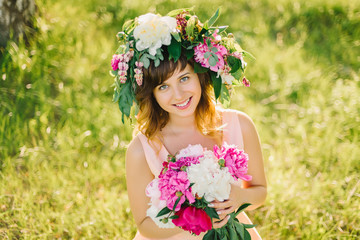 Fototapeta premium portrait of a happy smiling girl with a wreath of flowers and a bouquet of peonies in nature on a Sunny summer day