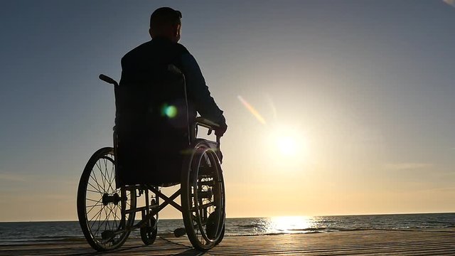 man in wheelchair silhouette near sea horizon panoramic shot