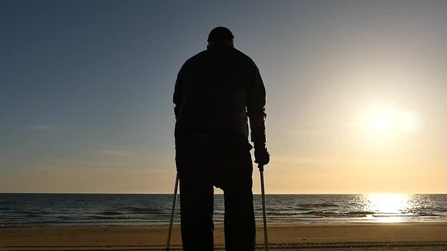 Disabled man silhouette with crutches on the beach panoramic shot