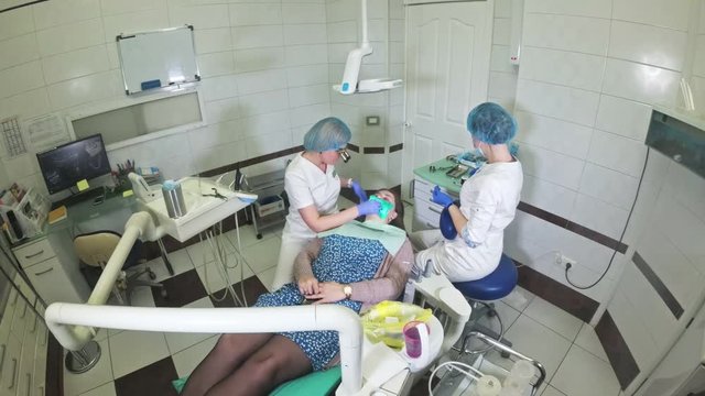 Woman at dentist clinic gets dental treatment to fill a cavity in a tooth. Dental restoration and composite material polymerization with UV light and laser. Shooting at a wide angle.