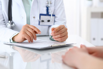 Doctor and patient talking while sitting at the desk in hospital office, closeup of human hands. Medicine and health care concept