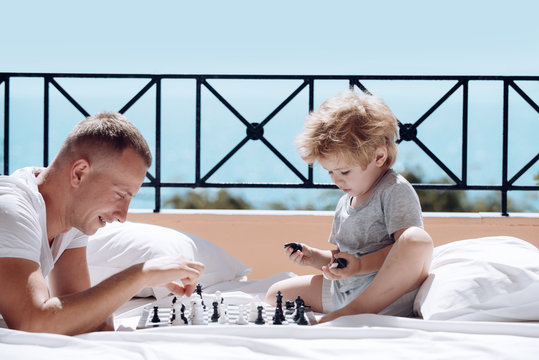 Smart toddler concept. Parent play chess with kid on terrace on sunny day. Dad with child play intellectual game. Father and little son play chess on balcony, nature and sea on background.