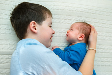 Big brother hugging his newborn baby girl. Toddler kid meeting new sibling