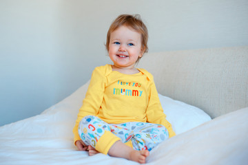 Funny little baby girl sitting in parents bed. Infant girl in yellow pajamas