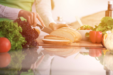 Closeup of human hands cooking in kitchen on the glass table with reflection Housewife slicing bread