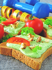 Fitness snack. Toasts with curd cheese, fresh herbs and tomatoes. Concept of healthy nutrition and sport. Dumbbells and measuring tape.