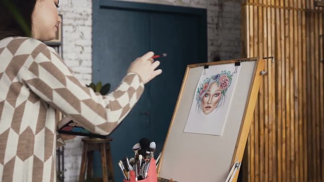 Young brunette woman in a bright studio draws a face chart. Makeup artist creates a beautiful face chart using shadows, lipsticks and blushes. A girl make-up artist learns to apply make-up using the