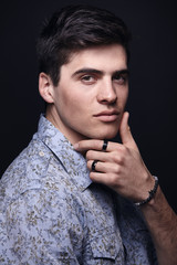 one young handsome model posing, wearing shirt, studio shot, black dark background.