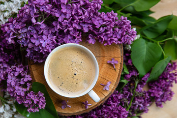 Obraz na płótnie Canvas spring background. coffee stands on a wooden hemp surrounded by lilac flowers 