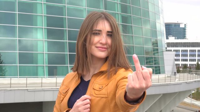 Very beautiful girl makes obscene hand gesture by showing middle finger in the city outdoor.
