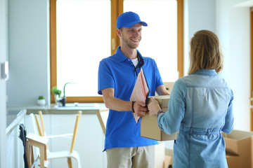 Smiling delivery man in blue uniform delivering parcel box to recipient - courier service concept. Smiling delivery man in blue uniform