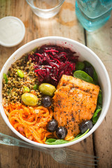 Salmon with spinach leaves, carrots, beetroots, grain edamame salad and black and green olives. Healthy fish and salad protein bowl