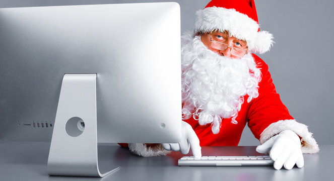 Santa Claus reading children letters and writing responses to them using laptop .