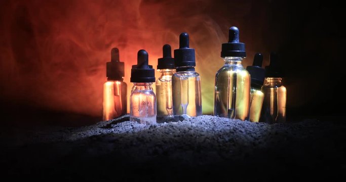Slider shot. Vape (Electronic cigarettes) concept. Smoke clouds and vape liquid bottles on dark toned background. Light effects. Useful as background or vape advertisement. Selective focus