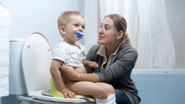 4k footage of happy young mother teaching her cute baby boy using toilet
