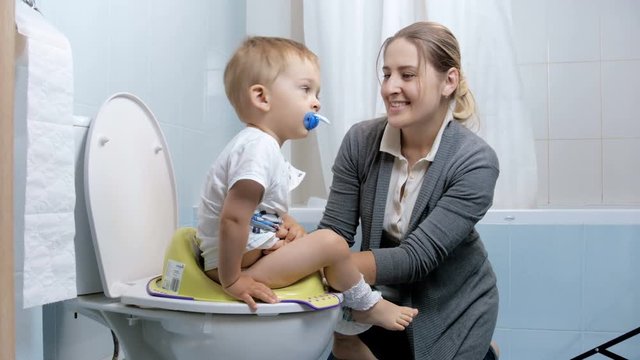 4k footage of young mother seating her baby son on toilet seat