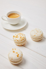 closeup shot of coffee cup and three macarons on white wooden table