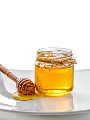 jar of honey with honey dipper  close-up on plate isolated on white background 
