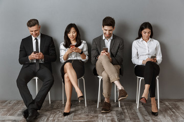 smiling interracial business people using smartphones while waiting for job interview