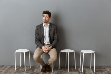 pensive businessman waiting for job interview on chair against grey wall