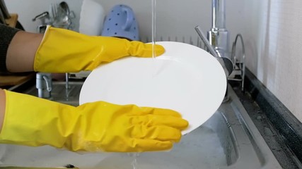 Closeup slow motion footage of housewife in yellow rubber gloves washing dishes in kitchen sink