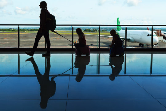 Mother with kids walk to flight boarding in airport transit hall and look through the window at airplane near departure gate. Active family lifestyle, travel by plane with children on summer vacation.